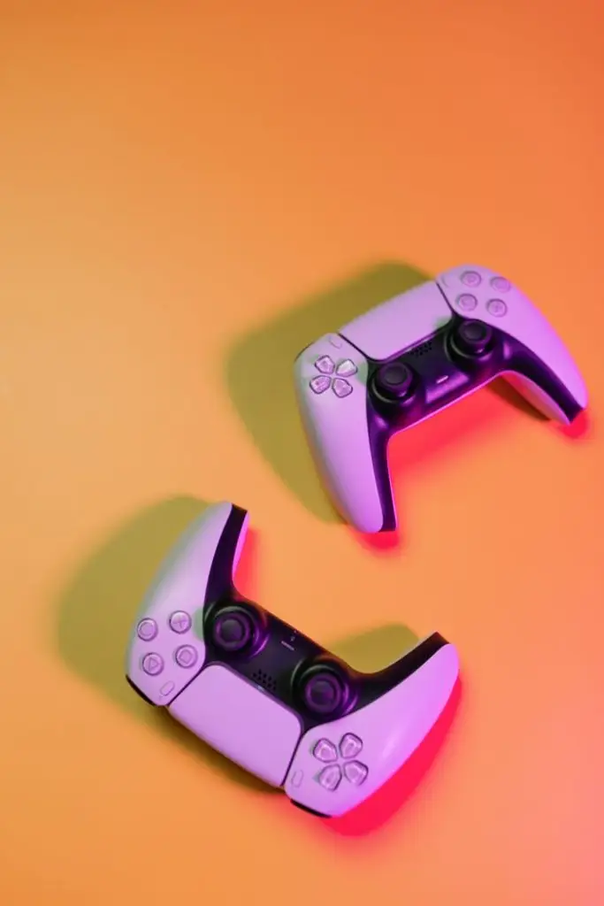 Two white video game controllers on an orange background, shot from above with colored lighting.